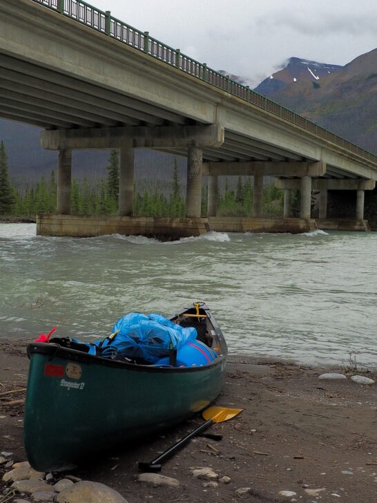 a canoe sits on a riverbank under an overpass
