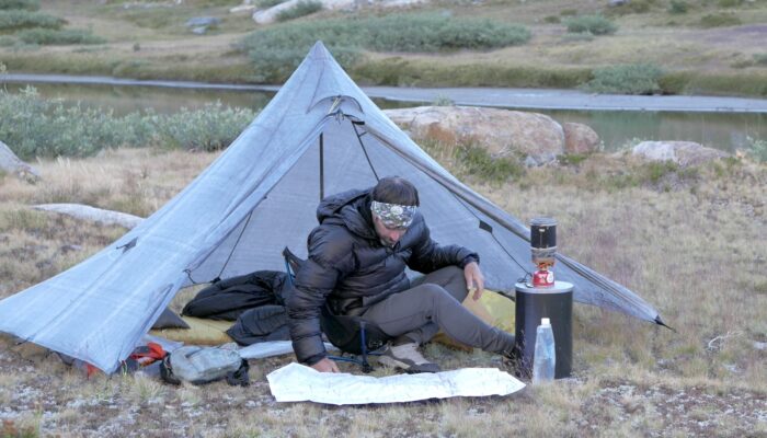 a man sitting in front of a tent on top of a field